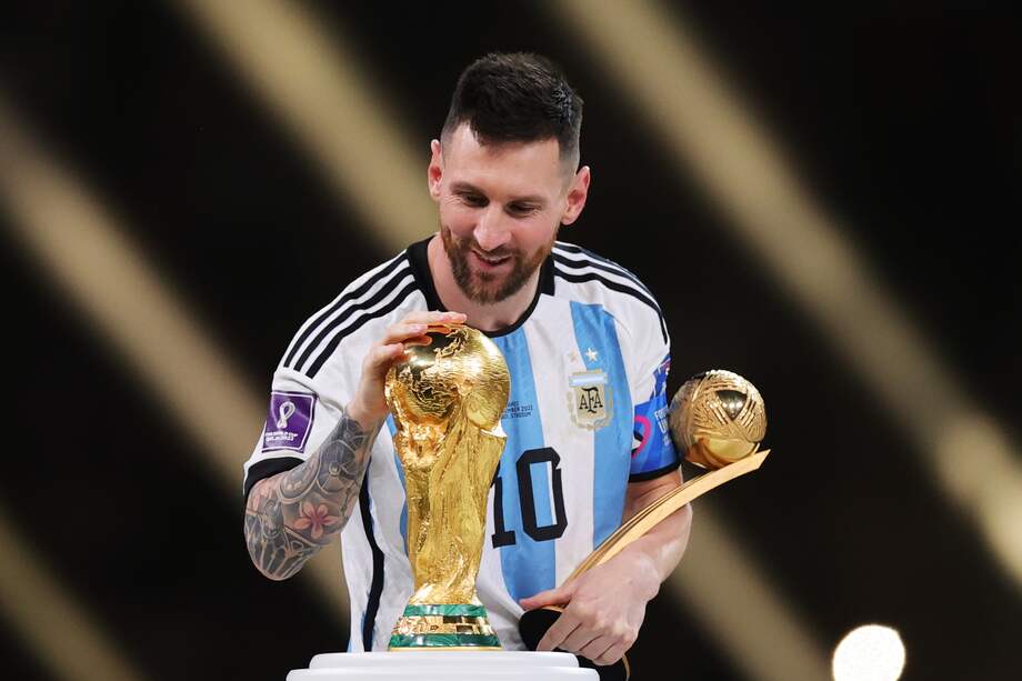 Messi mira la copa del mundo, mientras sostiene el premio al mejor jugador del Mundial en 2022.